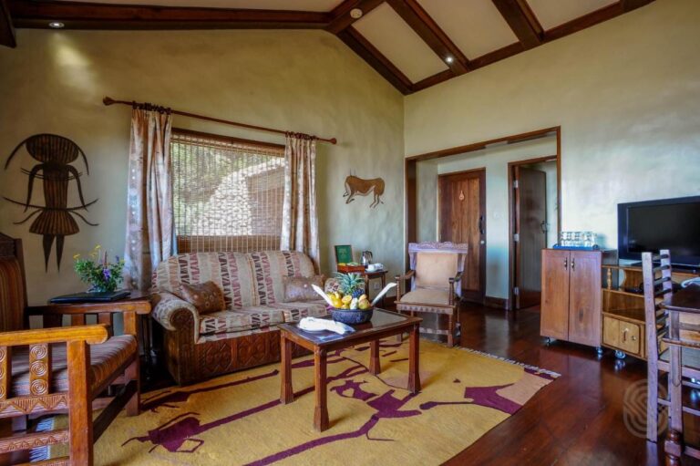 El salón de una suite, con sillones de madera tallada y una alfombra amarilla estampada