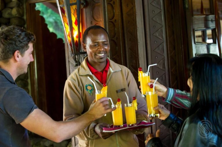 Un empleado del Ngorongoro Serena Safari Lodge ofrece una bandeja de zumos de fruta a dos viajeros