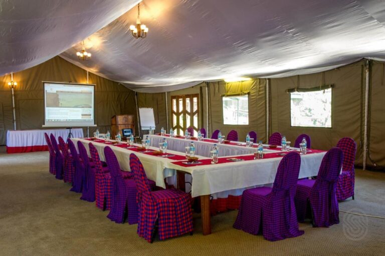 Una sala de reuniones bajo una carpa, con una mesa en U y sillas vestidas con tela a cuadros