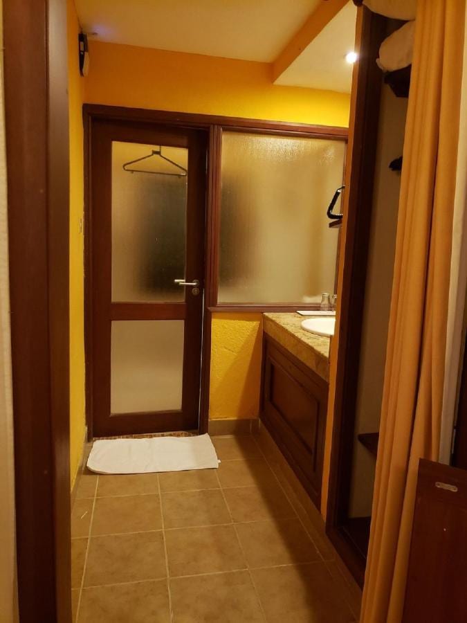 La entrada de un baño de paredes amarillas, con un lavabo y una puerta de vidrio esmerilado
