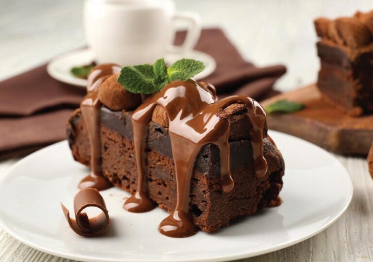 Un trozo de pastel de chocolate cubierto de salsa, con hojas de menta