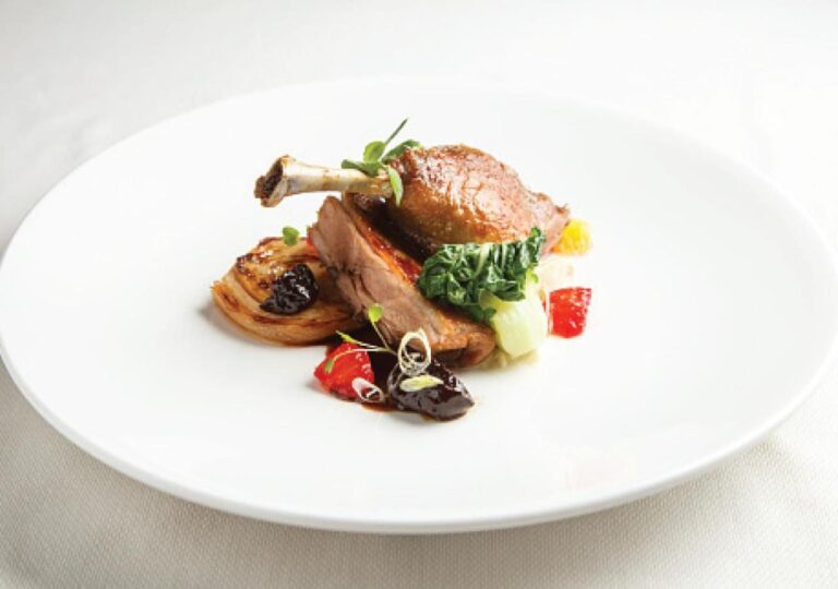 Un muslo de ave asado con sus verduras en un plato blanco