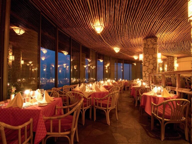 El comedor del restaurante iluminado con velas, con manteles rojos y sillones de ratán bajo un techo de madera