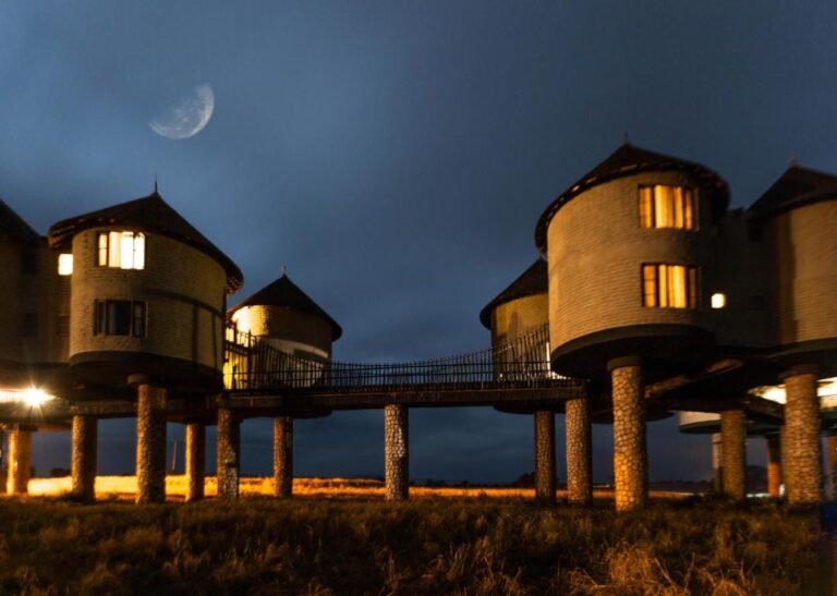 Dos torres iluminadas unidas por una pasarela, sobre sus pilares de piedra, bajo la luna