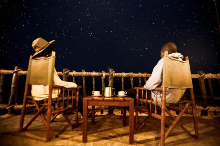 Dos personas sentadas en sillones de lona en la terraza, con dos tazas sobre la mesa, bajo un cielo estrellado