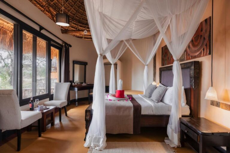 Una habitación con cama con dosel cubierta de mosquiteros blancos, con dos sillones delante de los ventanales