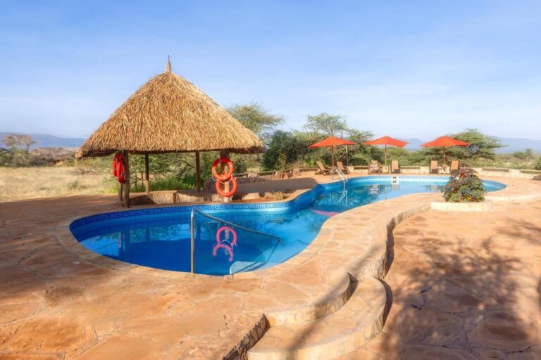 La piscina del Samburu Sopa Lodge, su palapa con flotadores naranjas y sus sombrillas rojas frente a la sabana