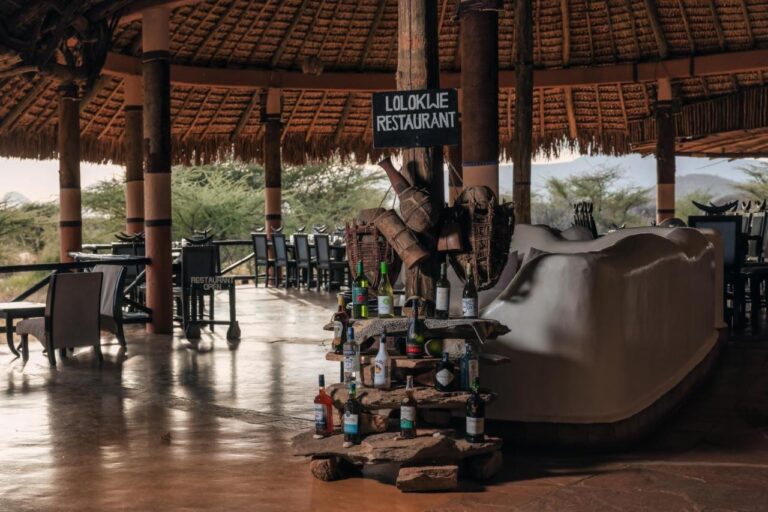 La entrada del restaurante Lolokwe, con botellas de vino sobre piedras, bajo un gran techo de paja