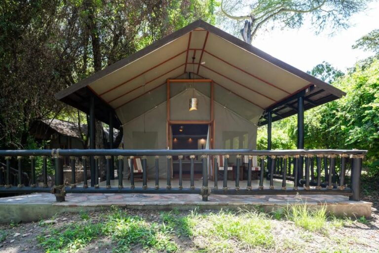 Una tienda del Sarova Mara Game Camp bajo su techo, sobre una terraza con barandilla, entre los árboles