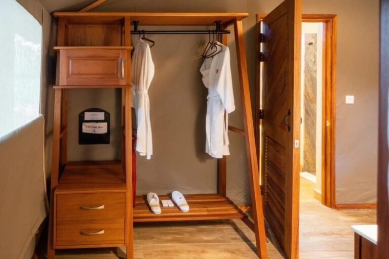 Un armario abierto con dos albornoces y zapatillas, junto a la puerta del baño