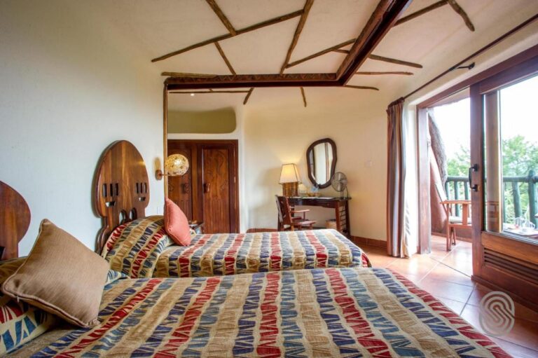 Una habitación con dos camas de cabeceros de madera calada, abierta a un balcón por una puerta de vidrio