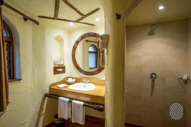 Un baño de paredes enlucidas, con un lavabo bajo un espejo redondo y una gran ducha de azulejos