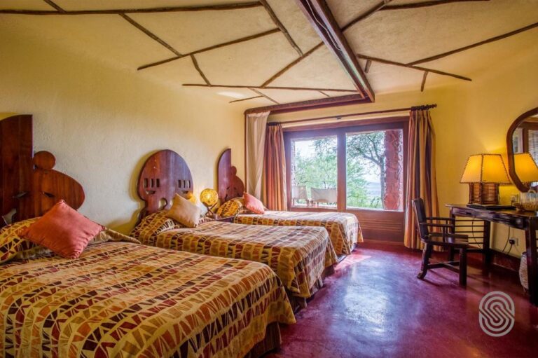 Una habitación con tres camas de cabeceros de madera tallada, sobre un suelo rojo encerado