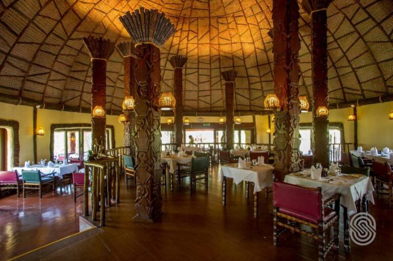 El comedor del restaurante bajo su cúpula, con columnas de madera talladas con figuras y mesas con manteles blancos