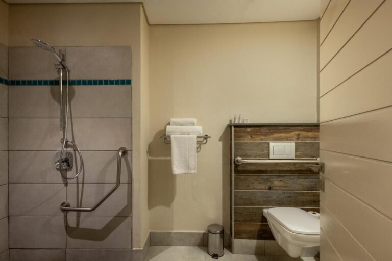 Un baño con ducha a ras de suelo, barras de apoyo e inodoro suspendido