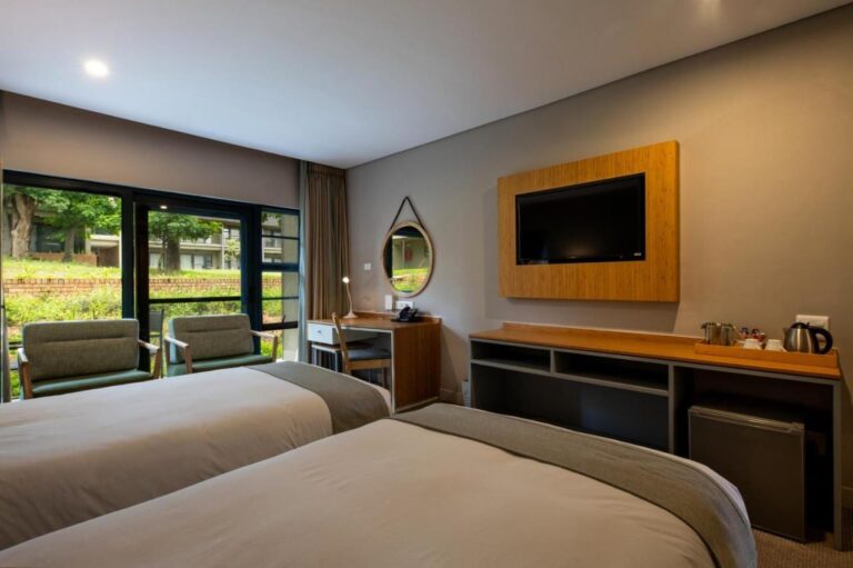 Una habitación con dos camas, televisión, hervidor y vista al jardín