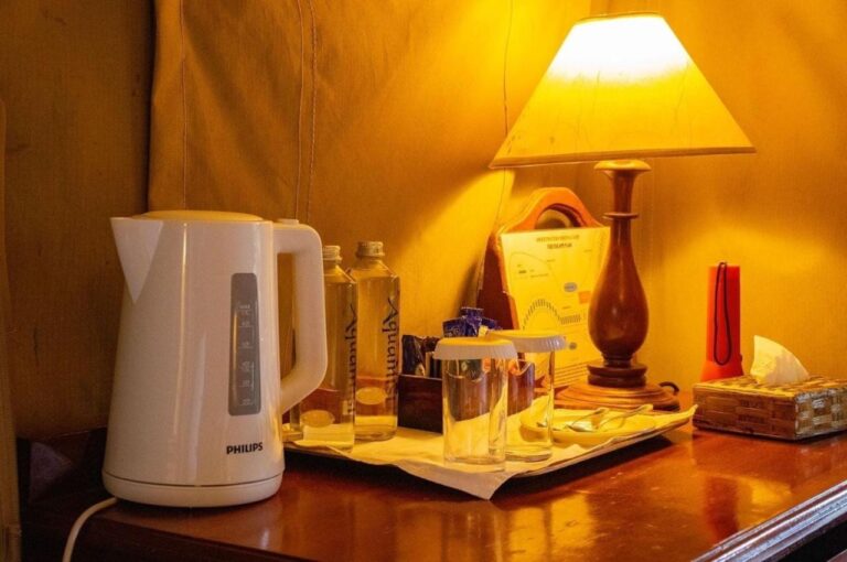 Un hervidor, botellas de agua y vasos sobre un escritorio, bajo una lámpara