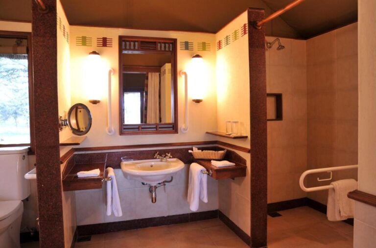 Un baño adaptado, con barras de apoyo, lavabo y ducha a ras de suelo