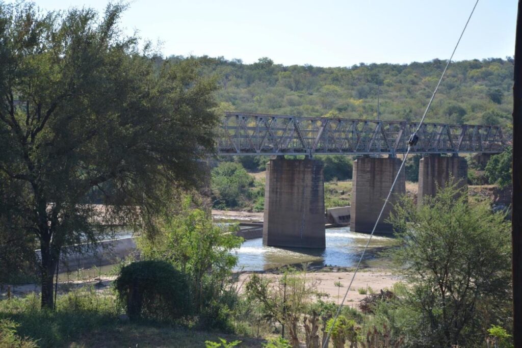 Un puente metálico sobre pilares de hormigón encima del río Olifants, visto desde el jardín del Three Bridges B&B