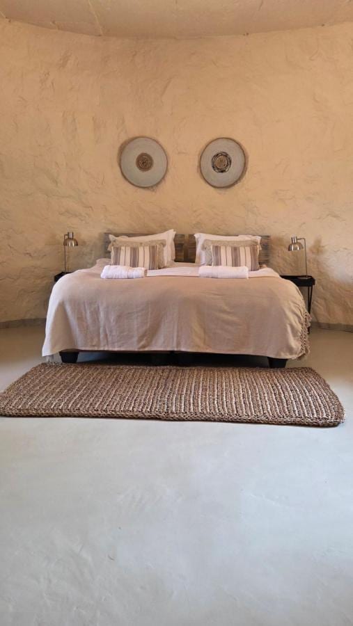 Una habitación de paredes redondeadas y enlucidas, con una cama grande, dos discos decorativos en la pared y una alfombra trenzada