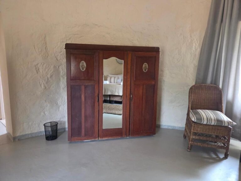 Un armario de madera oscura con puerta de espejo y un sillón de ratán, en una habitación de paredes enlucidas
