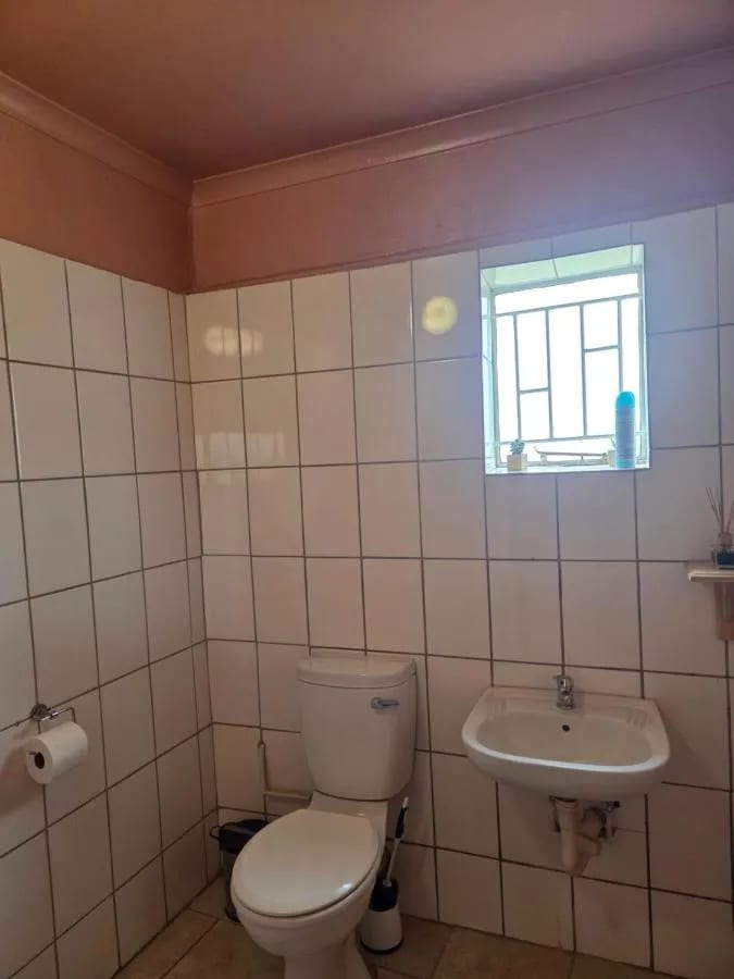 Un baño con azulejos blancos, con inodoro, lavabo y una ventana pequeña