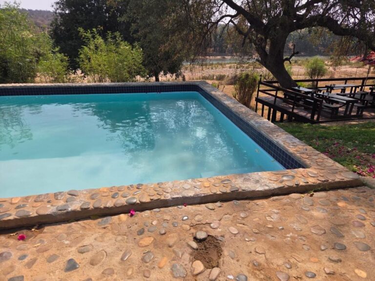 La piscina bordeada de cantos rodados del Three Bridges B&B, delante de una terraza de madera con mesas de picnic y el río