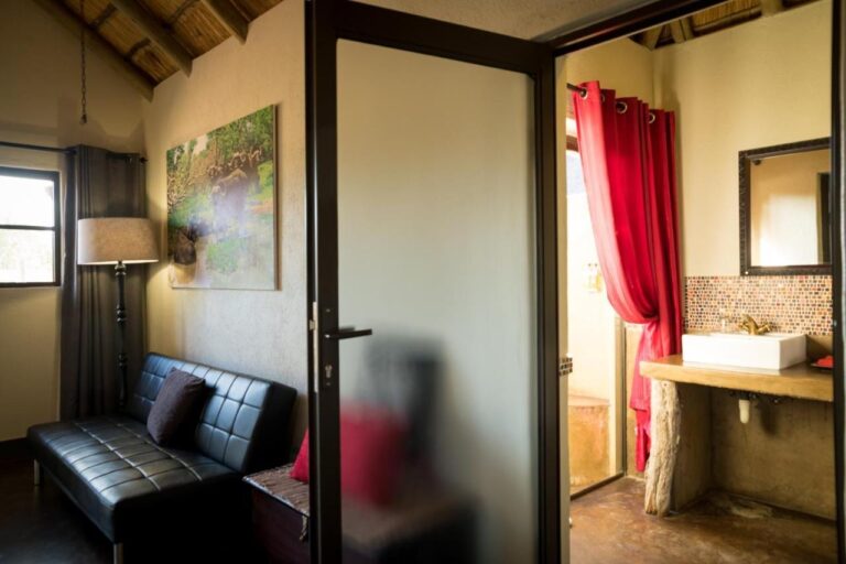 La zona de estar de una habitación, con un sofá de cuero negro, y el baño detrás de una puerta acristalada