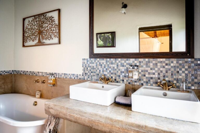 Un baño con dos lavabos sobre una encimera de hormigón, una bañera y un revestimiento de mosaico